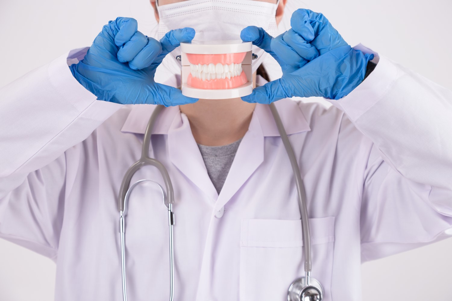 Foto de dentista segurando prótese dentária à frente do rosto (que está com máscara)..