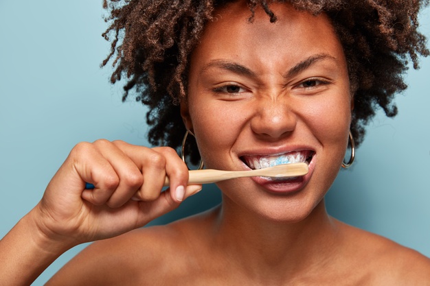 Fotografia de uma mulher preta de cabelos encaracolados escovando os dentes com uma escova biodegradável.