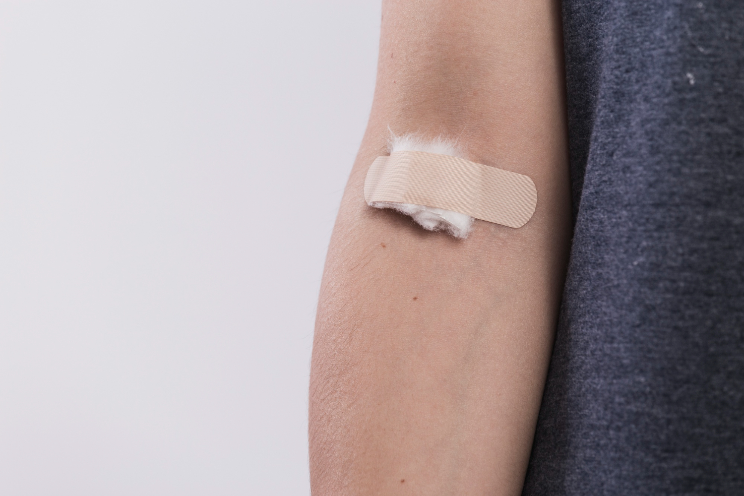 Close no braço de alguém que está com um band-aid e algodão após um exame de sangue.