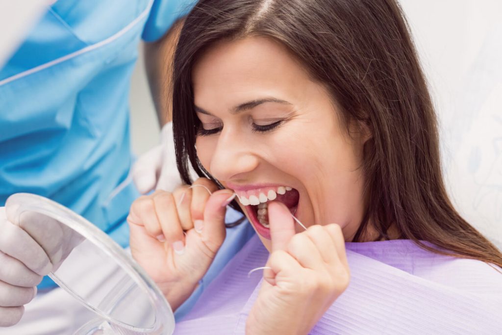 Fotografia de mulher em um consultório de dentista passando fio dental.