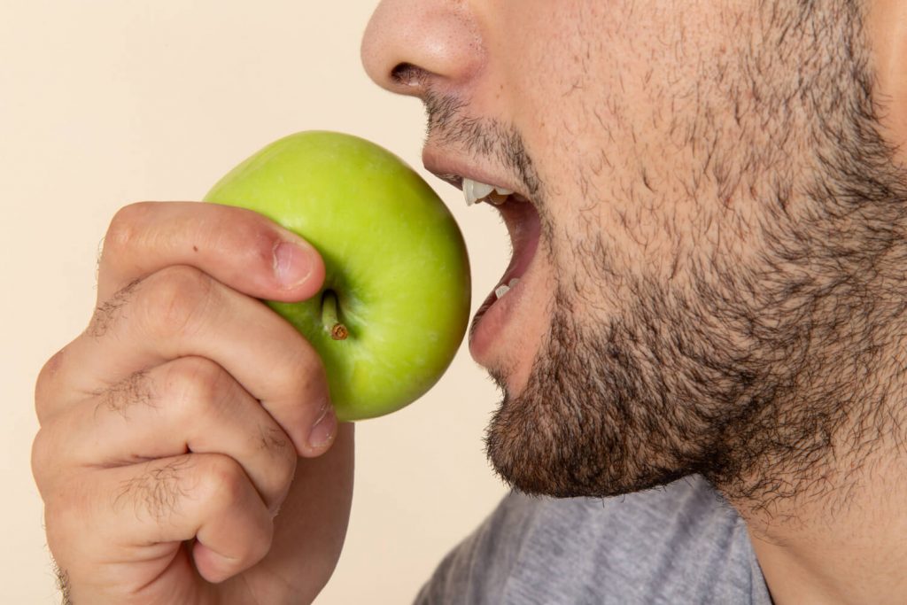 Fotografia colorida de homem prestes a morder uma maçã verde.
