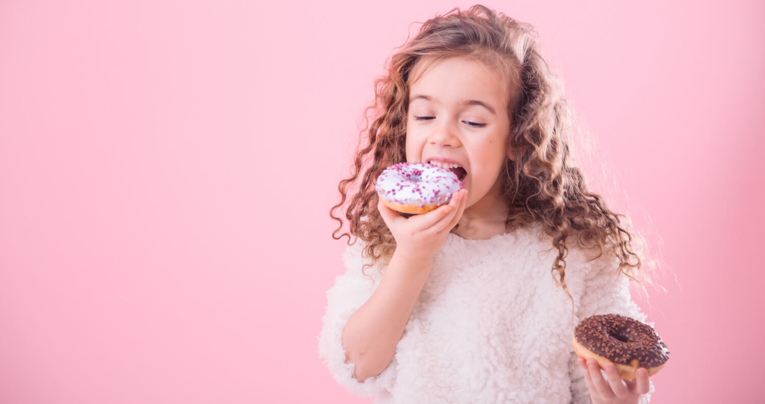 Foto colorida de uma menina comendo rosquinhas açucaradas.