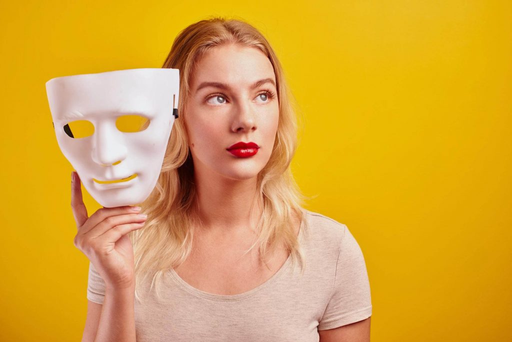 Pessoa feminina loira segurando uma máscara artística.