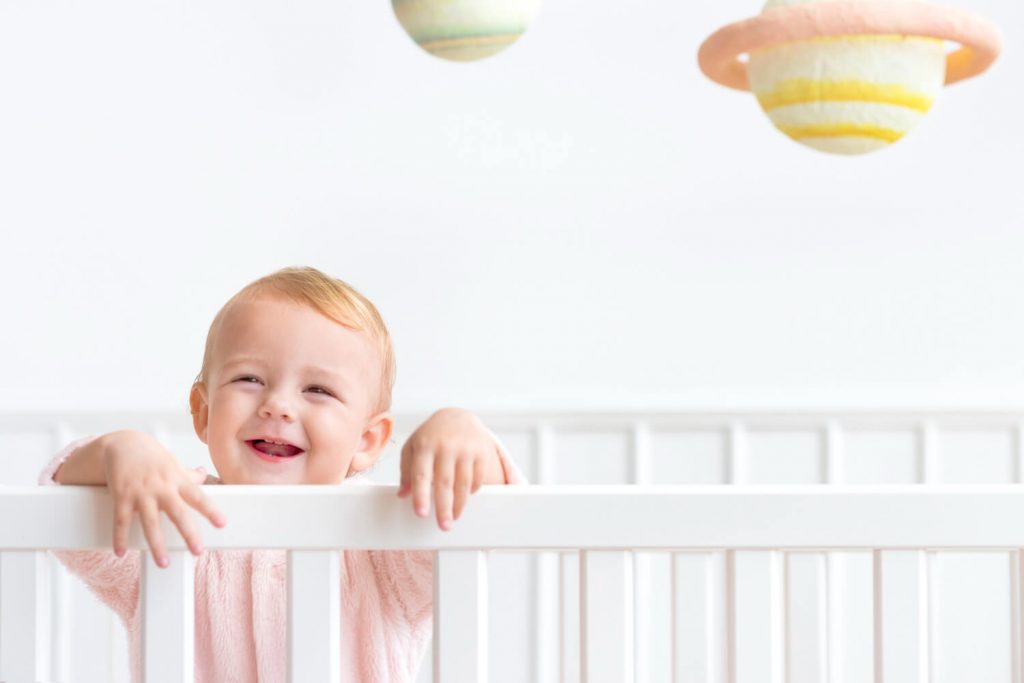 Fotografia de bebê sorridente dentro de berço branco.